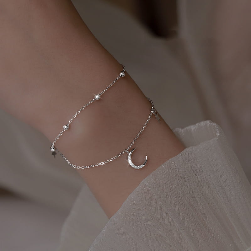 A delicate double layer silver anklet bracelet featuring a crescent moon charm and small star-shaped crystal beads.