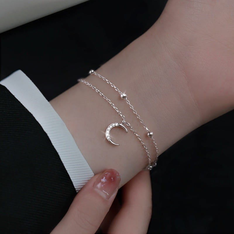 Delicate silver double-layer anklet bracelet featuring a crescent moon charm with sparkling stones and small spherical beads.