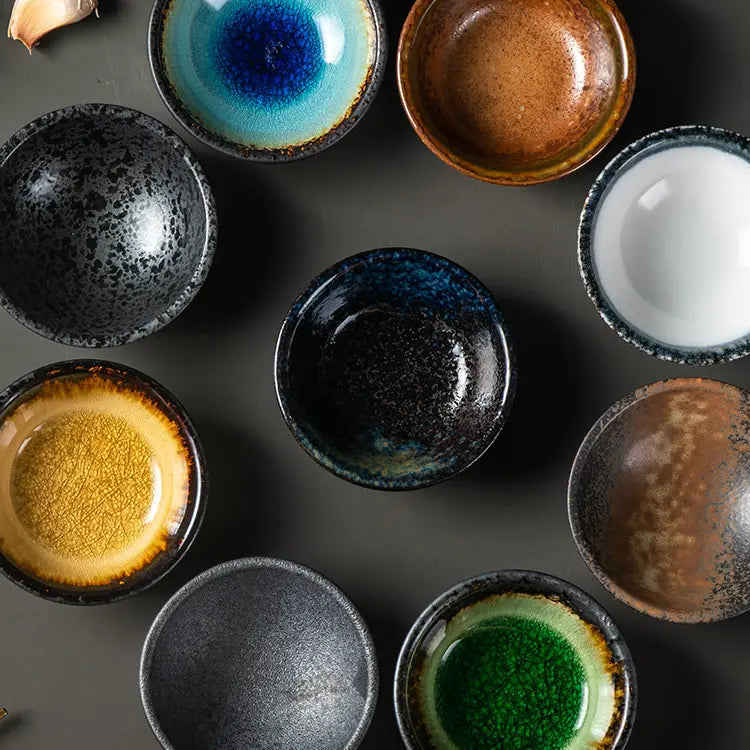 A collection of Japanese ceramic small plates featuring rustic speckled glaze with vibrant blue brown black white yellow and green colors.