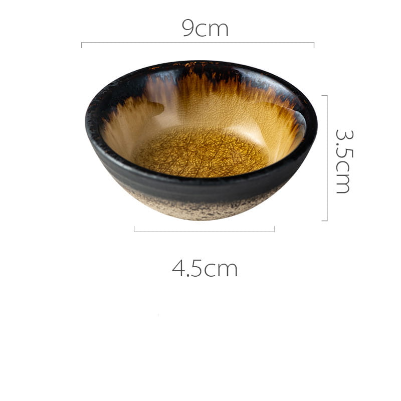 A Japanese ceramic small plate with a rustic speckled glaze featuring a glossy black rim and interior and a golden-brown crackled finish transitioning to a speckled beige base.