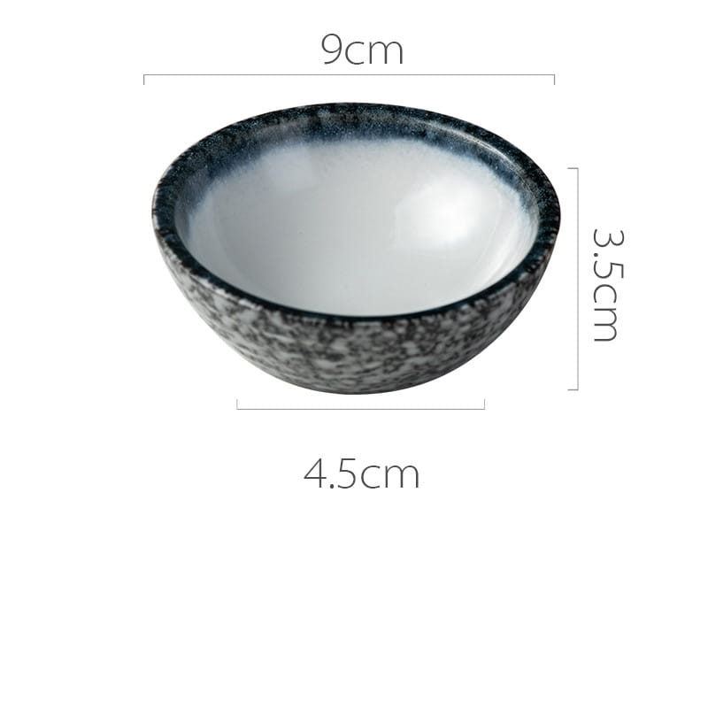 A sleek round ceramic vessel sink with a speckled black and gray exterior and a smooth white interior featuring a Japanese ceramic small plates rustic speckled glaze design.