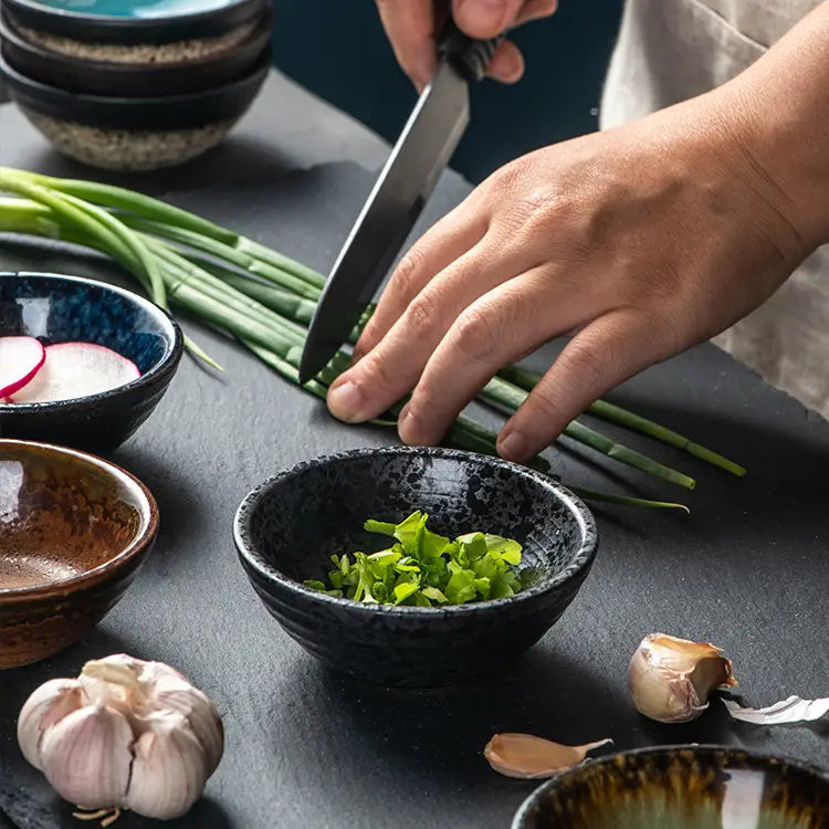 Black ceramic small plate with rustic speckled glaze holding chopped green herbs.