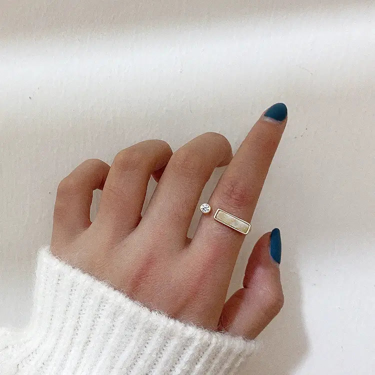 A delicate vintage geometric zircon marble adjustable ring with a gold band featuring a small round diamond and a rectangular light-colored stone.