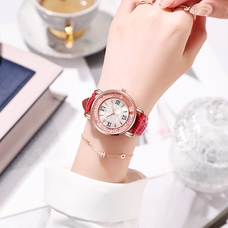 A delicate rose gold quicksand crystal watch featuring a sparkling crystal bezel, roman numeral hour markers on a white dial, and vibrant red embossed leather straps.