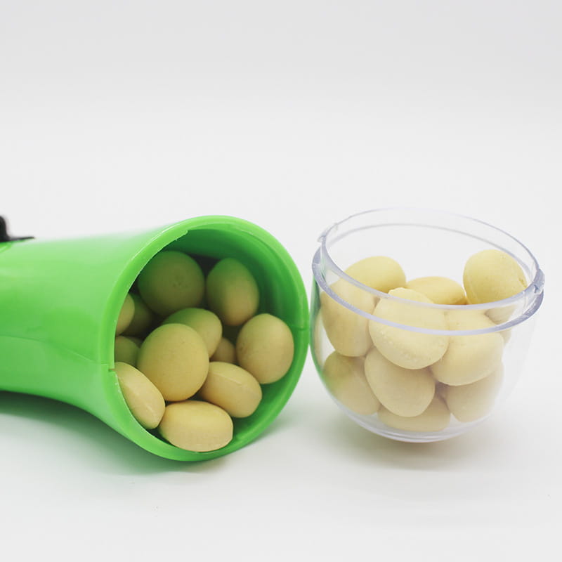 Boîte en plastique verte pour le lanceur de friandises pour chien, jouet portatif pour friandises pour animaux, remplie de bonbons ovales de couleur jaune clair.
