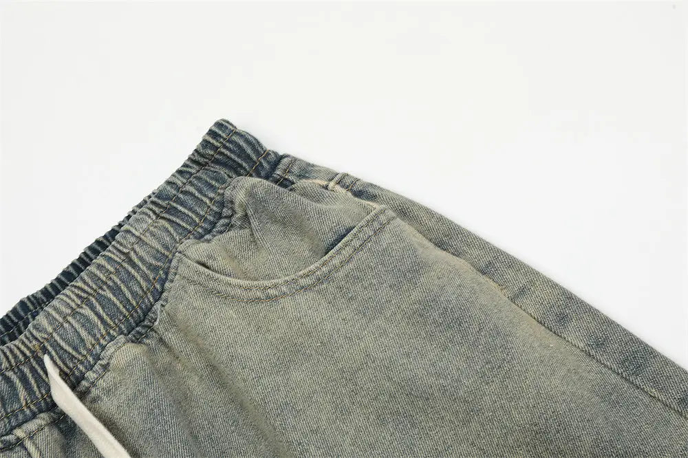 Joggers en denim clair pour hommes, avec ceinture élastique et cordon blanc, arborant un design à bretelle diagonale.