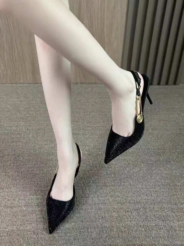 Black rhinestone slingback stiletto heels featuring black sparkly pointed toes and a gold-tone medallion accent.