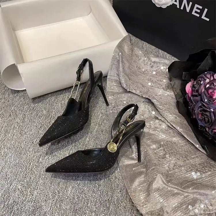 Black rhinestone slingback stiletto heels featuring black crystal embellishments with a gold-tone circular buckle and a slender high heel.