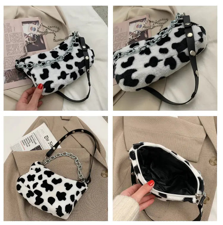 A plush black and white cow print crossbody baguette bag made of soft material with a silver chain strap.