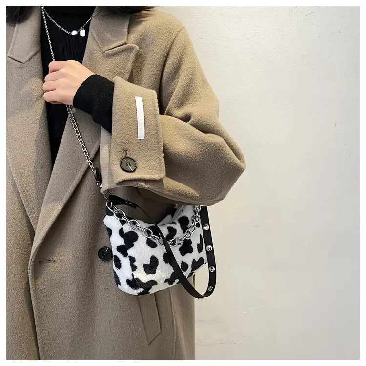 A black and white plush animal print baguette bag with a silver chain strap featuring a cow print crossbody design.