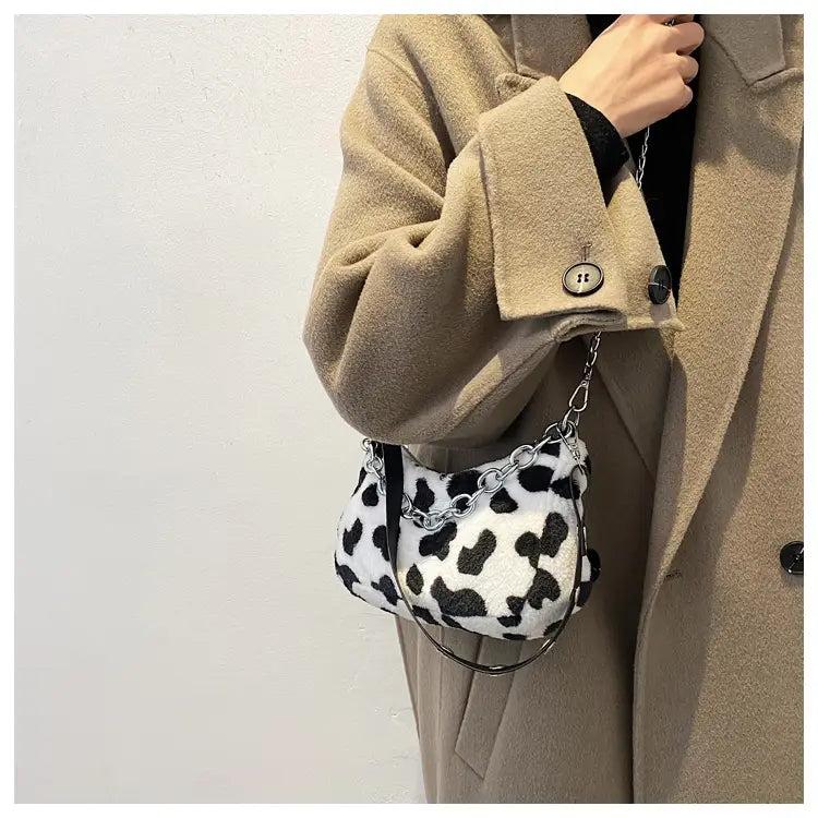 Plush animal print baguette bag featuring a black and white cow print faux fur with a silver chain strap.