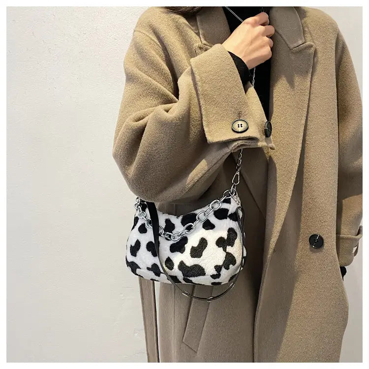 Plush animal print baguette bag in white and black cow print faux fur with a silver chain strap.