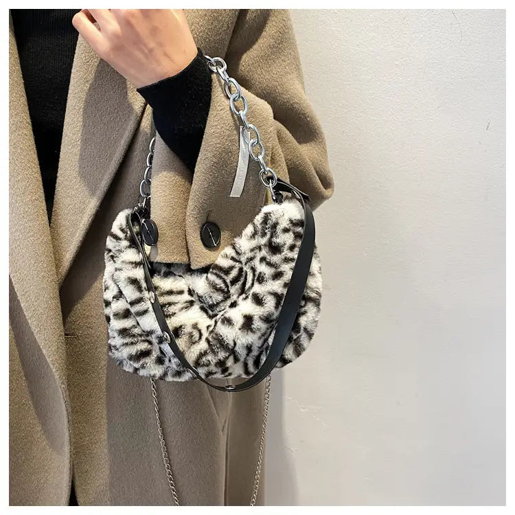 A stylish black and white leopard-print faux fur baguette bag with a silver chain strap for crossbody wear.