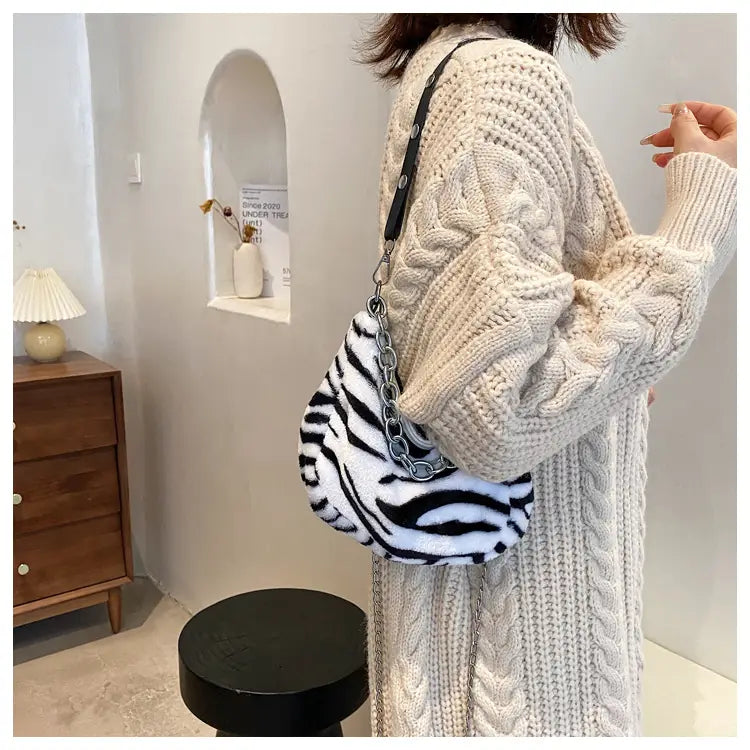 A plush black and white zebra-striped animal print baguette bag with a silver chain strap made of soft fabric.