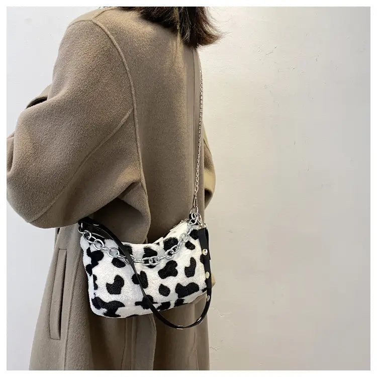 Plush animal print baguette bag featuring a white and black cow print faux fur with a silver chain strap for crossbody use.