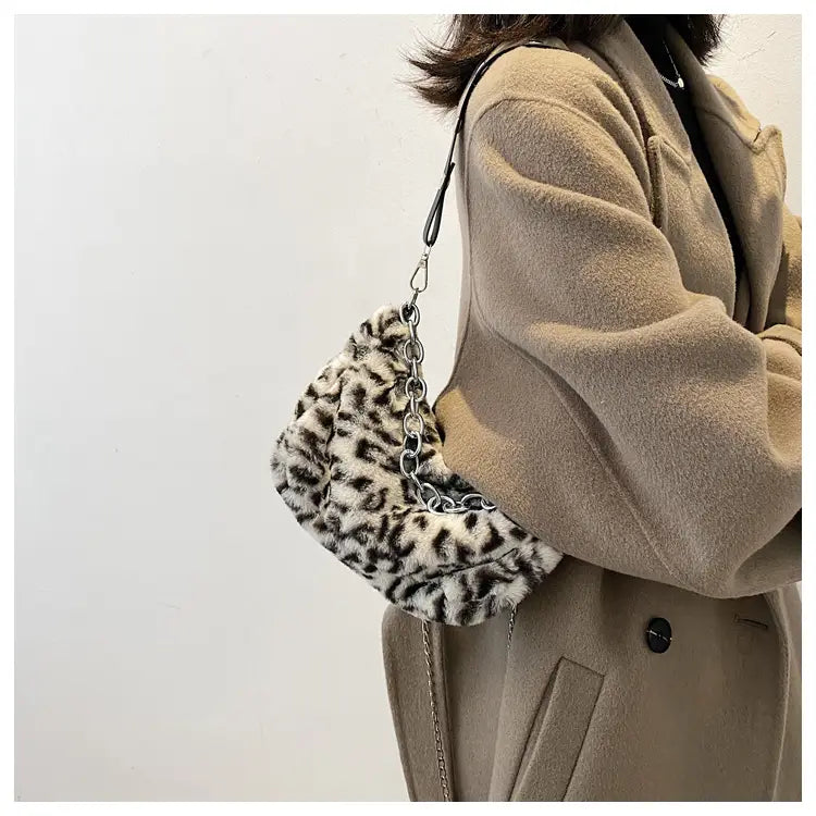Plush animal print baguette bag featuring faux fur leopard print and a silver chain strap for crossbody use.