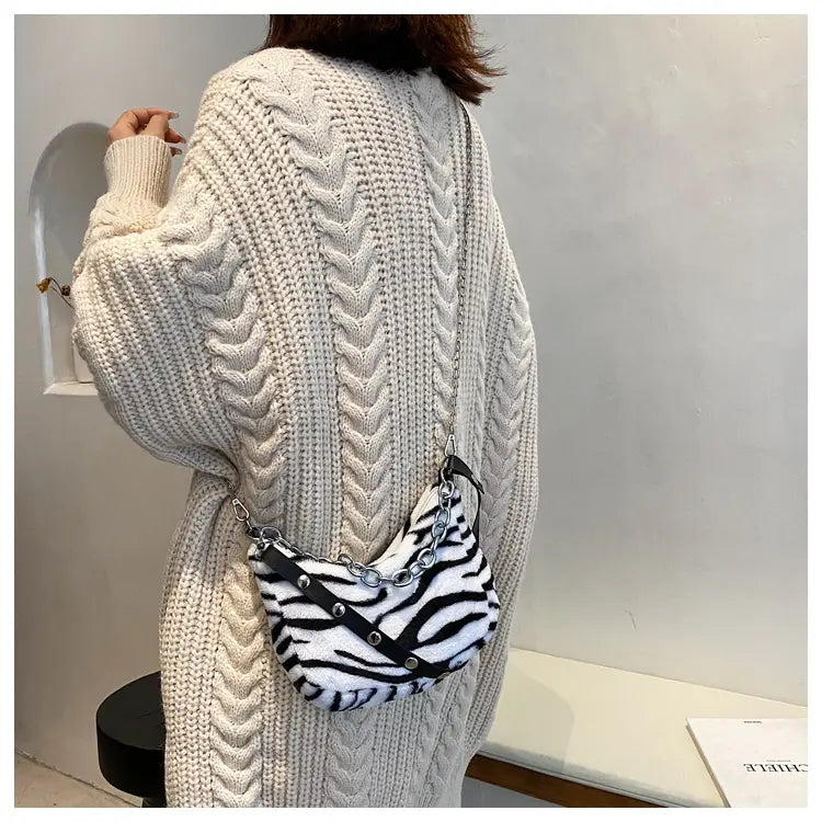 A black and white zebra-striped plush animal print baguette bag with a silver chain strap designed as a crossbody accessory.