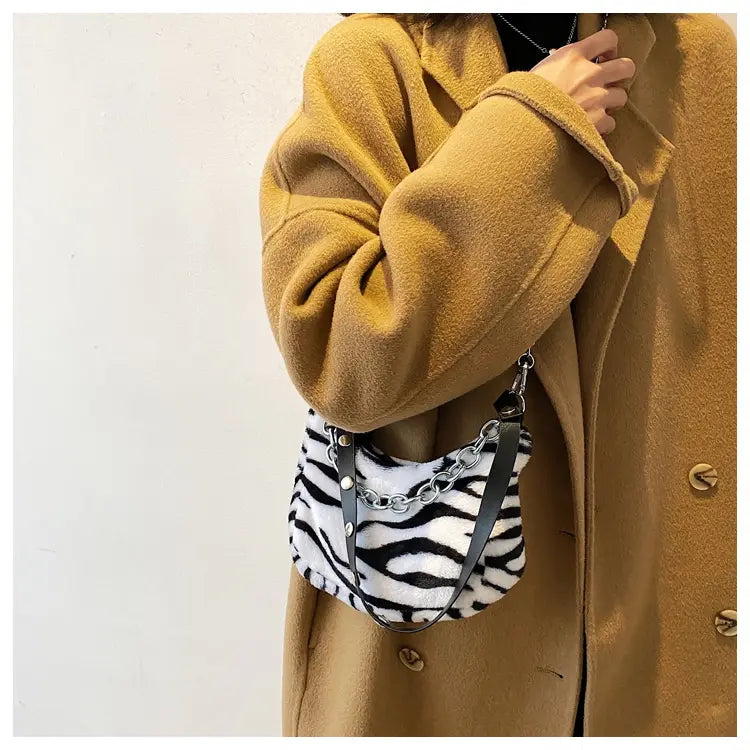 A plush black and white zebra-striped crossbody bag with a silver chain strap designed as an animal print baguette bag.