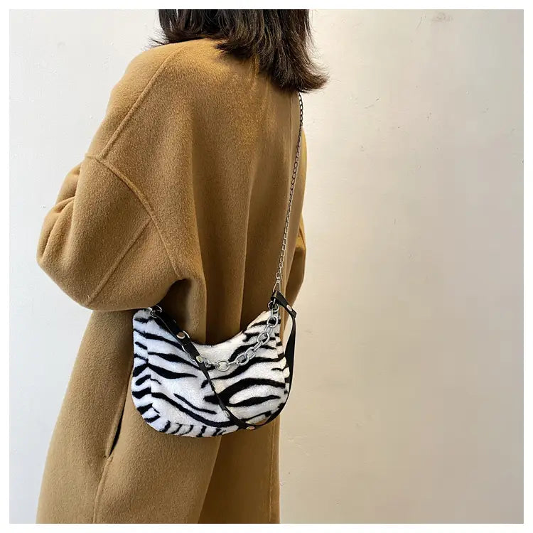 A plush black and white zebra-striped crossbody baguette bag with a silver chain strap made from soft fabric.