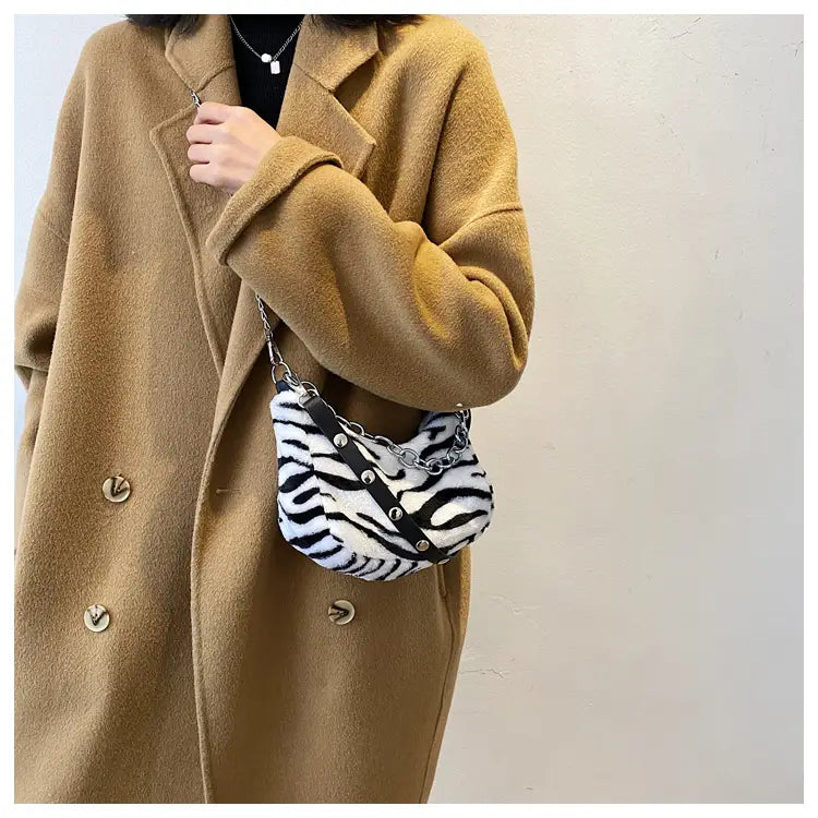 A plush zebra-striped animal print baguette bag featuring a silver chain and leather crossbody strap.