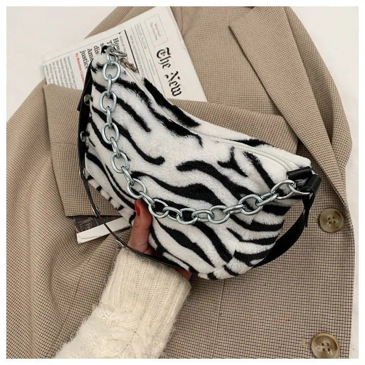 A plush black and white zebra-striped fanny pack with a silver chain strap featuring a soft animal print design.