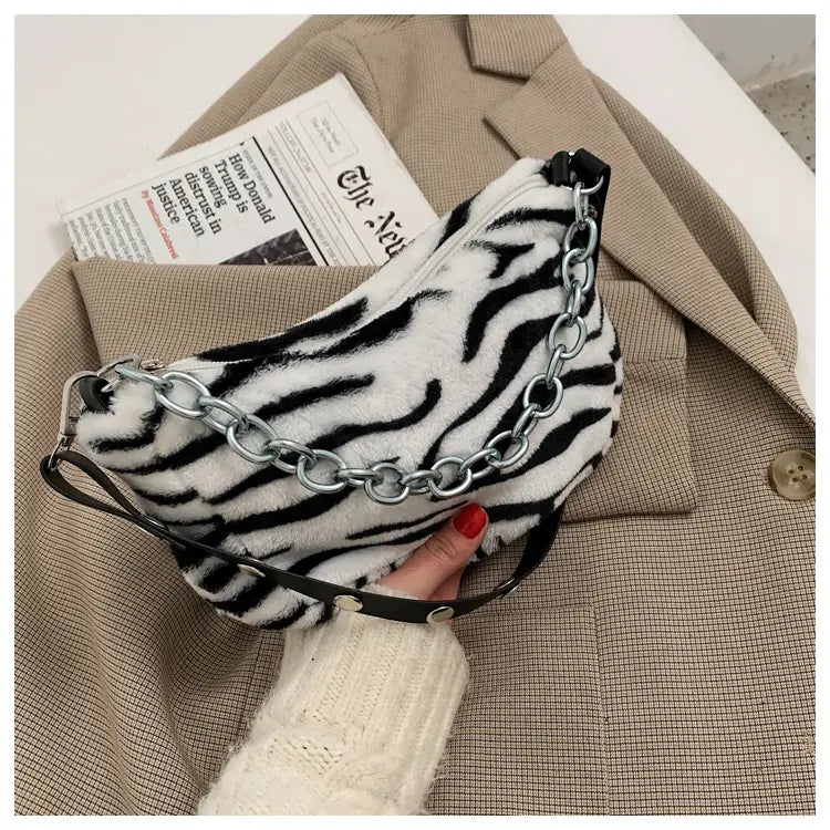 A plush black and white zebra-striped baguette bag with a silver chain strap made of soft material.