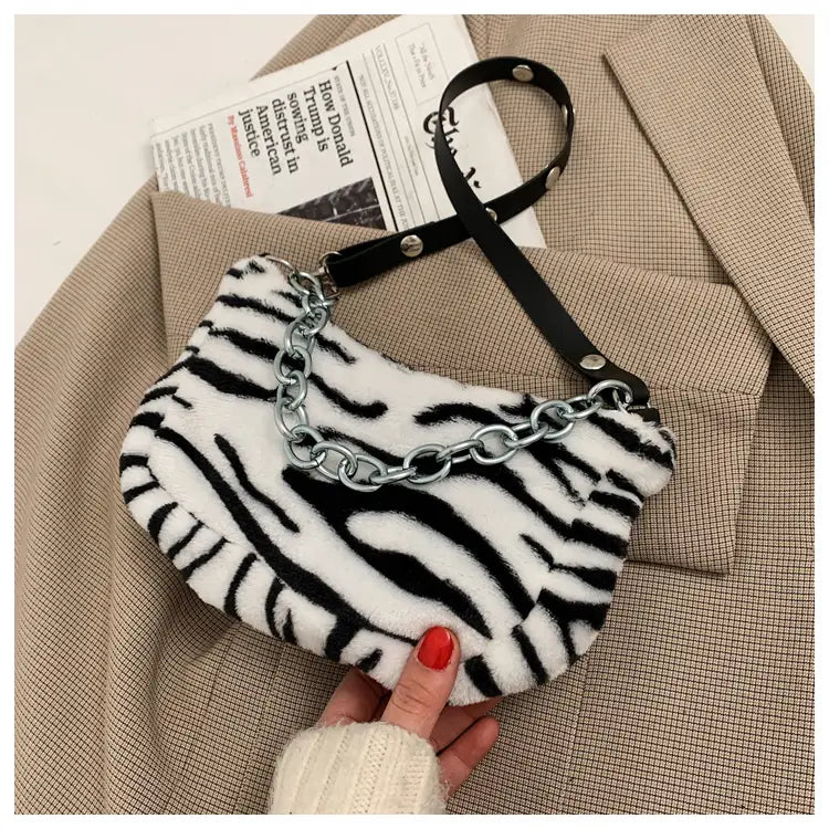 A plush animal print baguette bag featuring white and black zebra stripes with a silver chain strap and black leather handle.