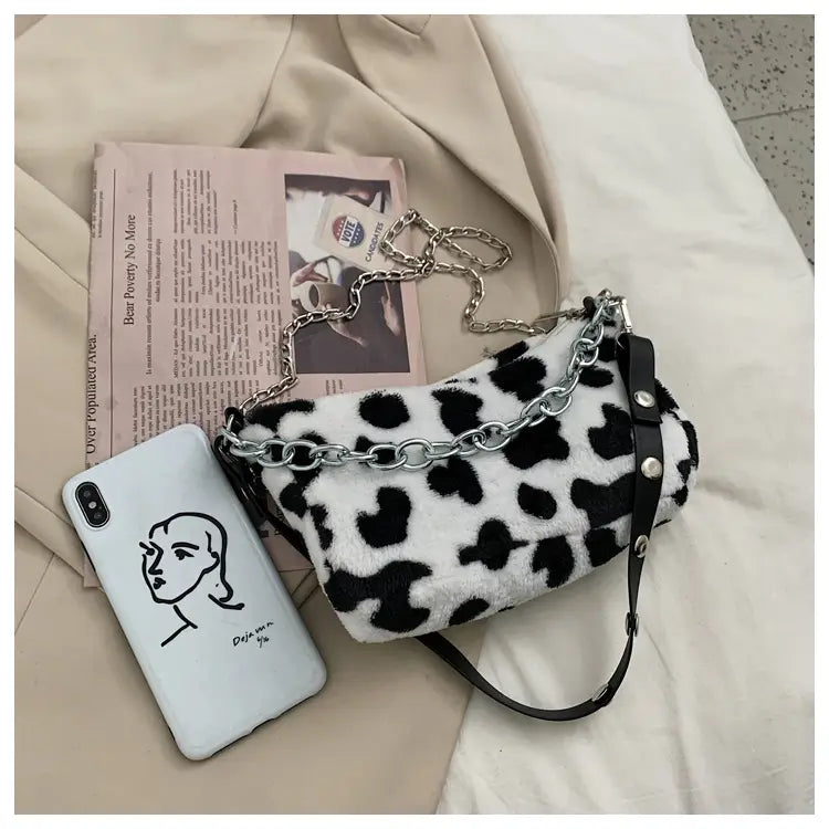 A plush black and white leopard print baguette bag with a silver chain strap and crossbody style.