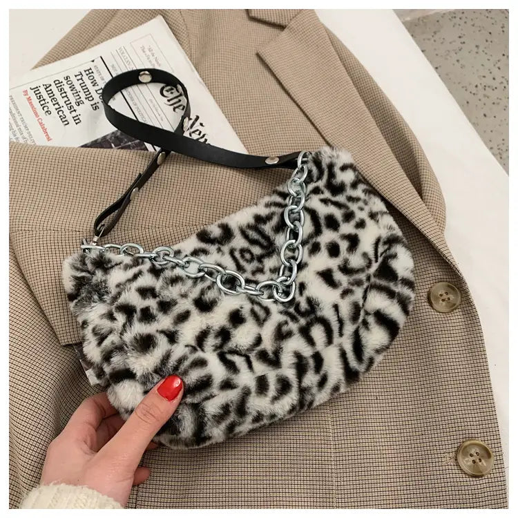 A black and white leopard-print faux fur baguette bag with a silver chain strap designed as a crossbody accessory.