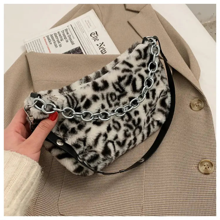 A black and white leopard-print faux fur plush animal print baguette bag with silver chain strap designed as a crossbody accessory.
