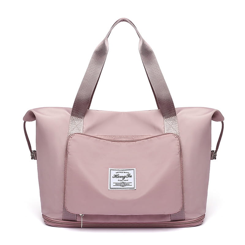 A soft pink lightweight foldable gym bag made of waterproof material with gray reinforced handles and a branded patch on the front designed as a travel duffel with a shoe pocket.