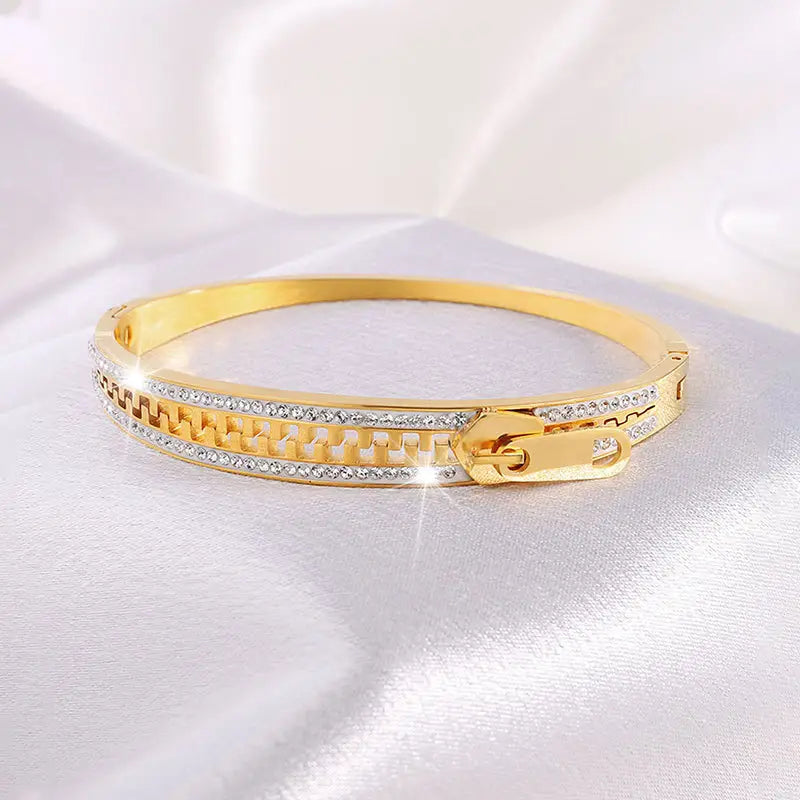 Gold-toned crystal interlocking titanium steel bangle bracelet featuring a zipper-style clasp and two rows of clear crystals in an intricate geometric pattern.