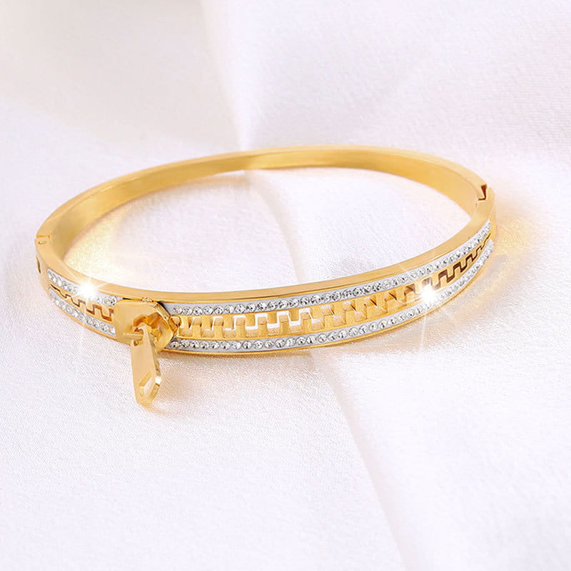Gold-toned crystal interlocking titanium steel zipper bangle bracelet with a sleek hinged design and two rows of sparkling clear crystals set along its inner edge.