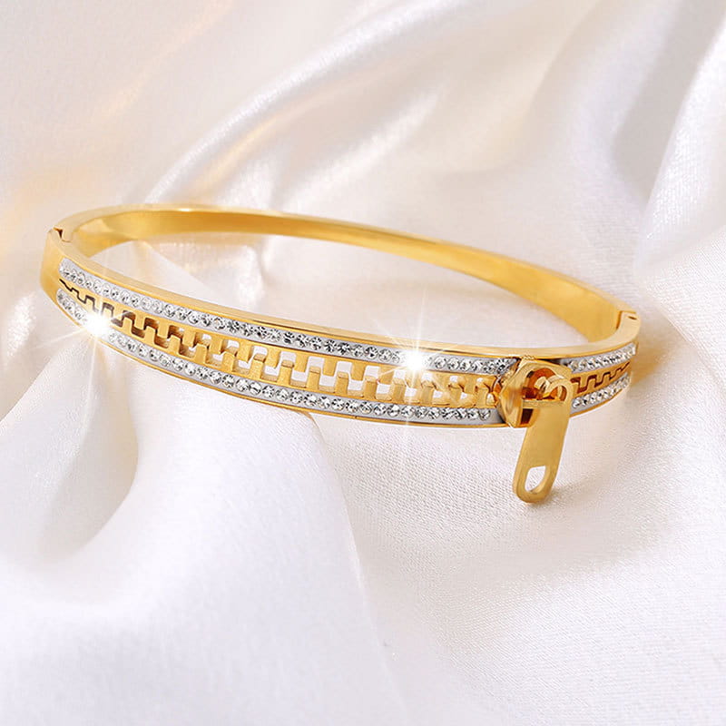 Gold-toned crystal interlocking titanium steel bangle bracelet featuring a zipper closure and two rows of clear crystals in an intricate geometric pattern.