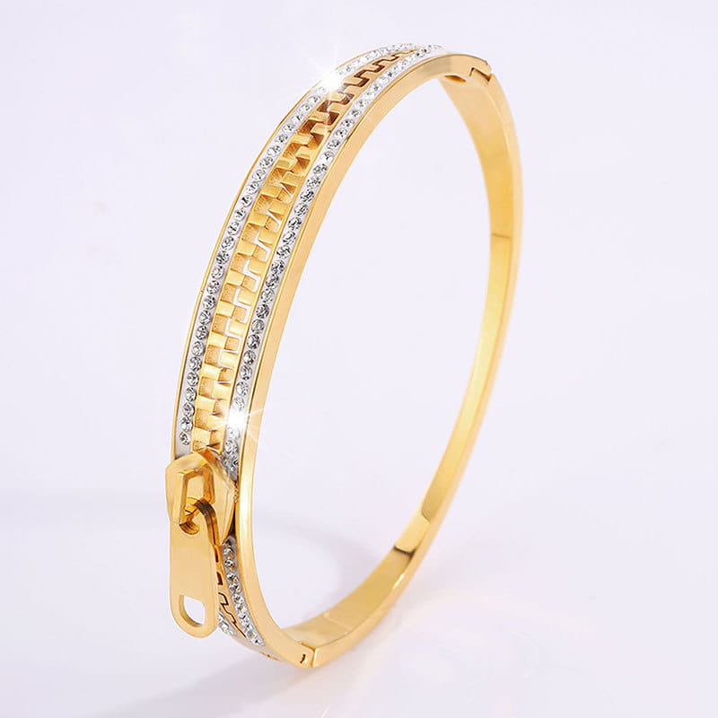 Gold-toned titanium steel bangle bracelet with a zipper design and embedded clear crystals along its length.