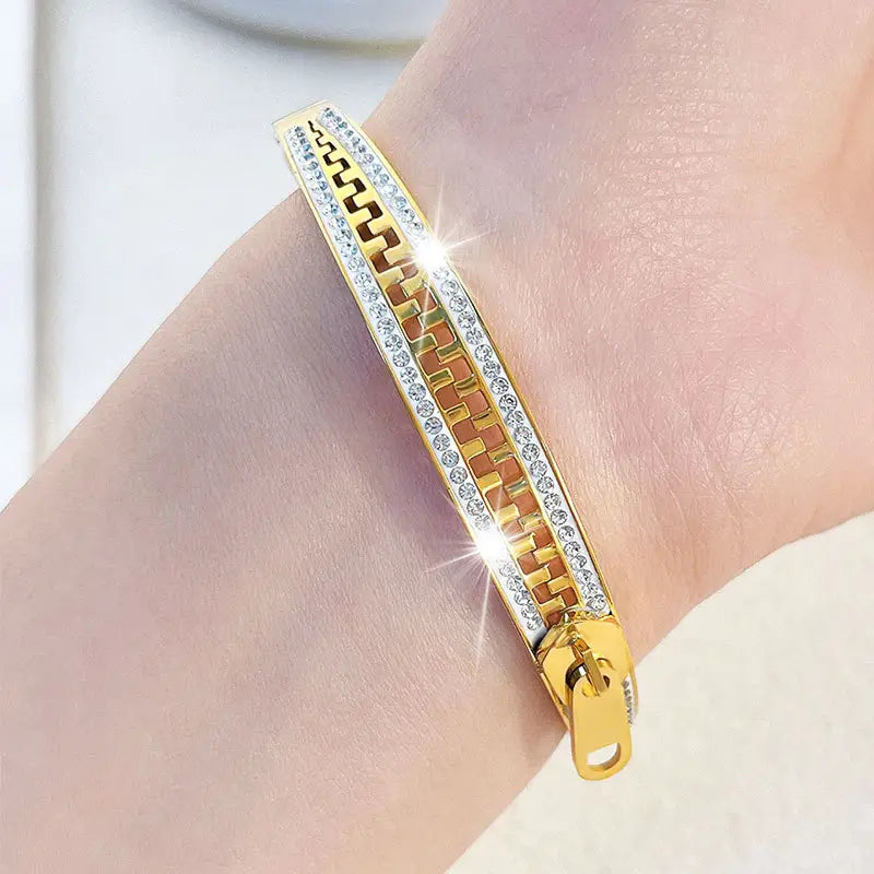 Gold-toned crystal interlocking titanium steel zipper bangle bracelet featuring a geometric pattern with clear crystals embedded along its edges.
