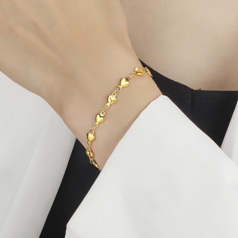 A delicate gold-colored polished gold heart link bracelet in titanium steel featuring small heart-shaped links connected by fine chains.