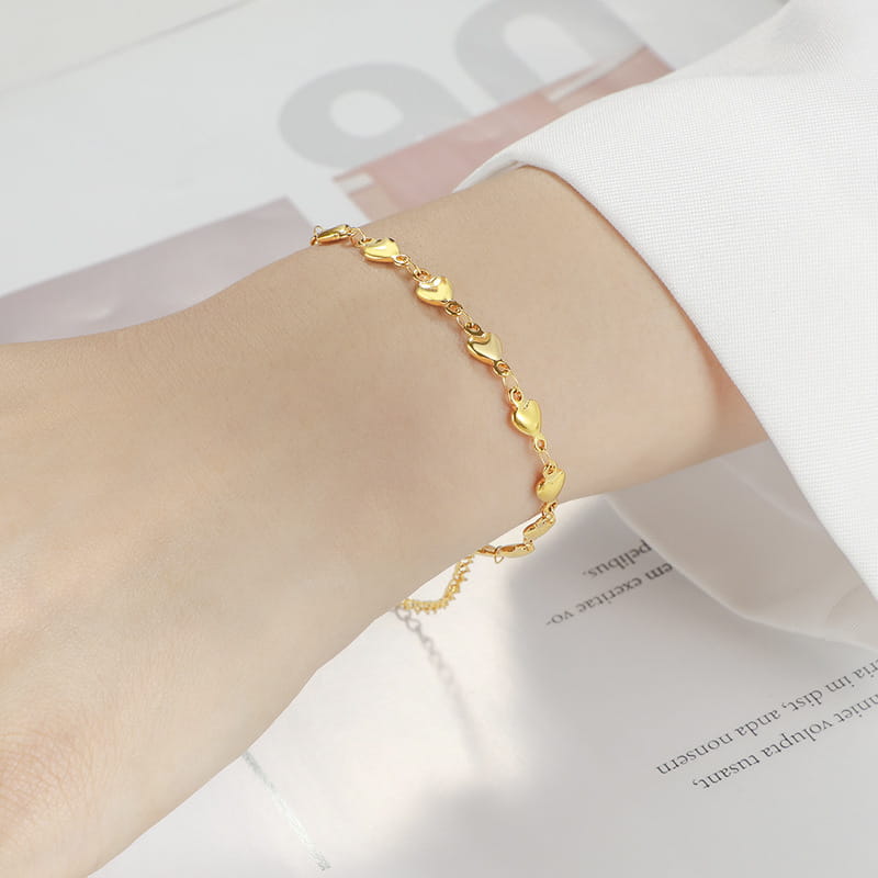 A polished gold heart link bracelet in titanium steel delicately worn on a wrist.