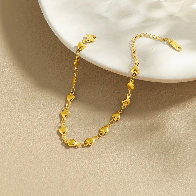 A polished gold heart link bracelet made of titanium steel featuring a delicate chain of small heart-shaped links.