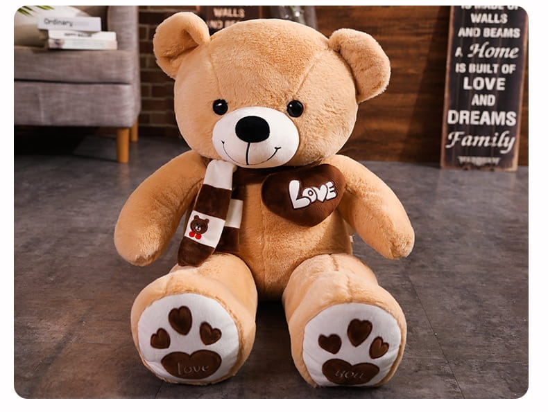 A plush tan teddy bear soft stuffed animal doll with a white snout, black button eyes and nose, wearing a brown and white striped scarf and holding a heart-shaped love charm measuring 60 to 100 centimeters.