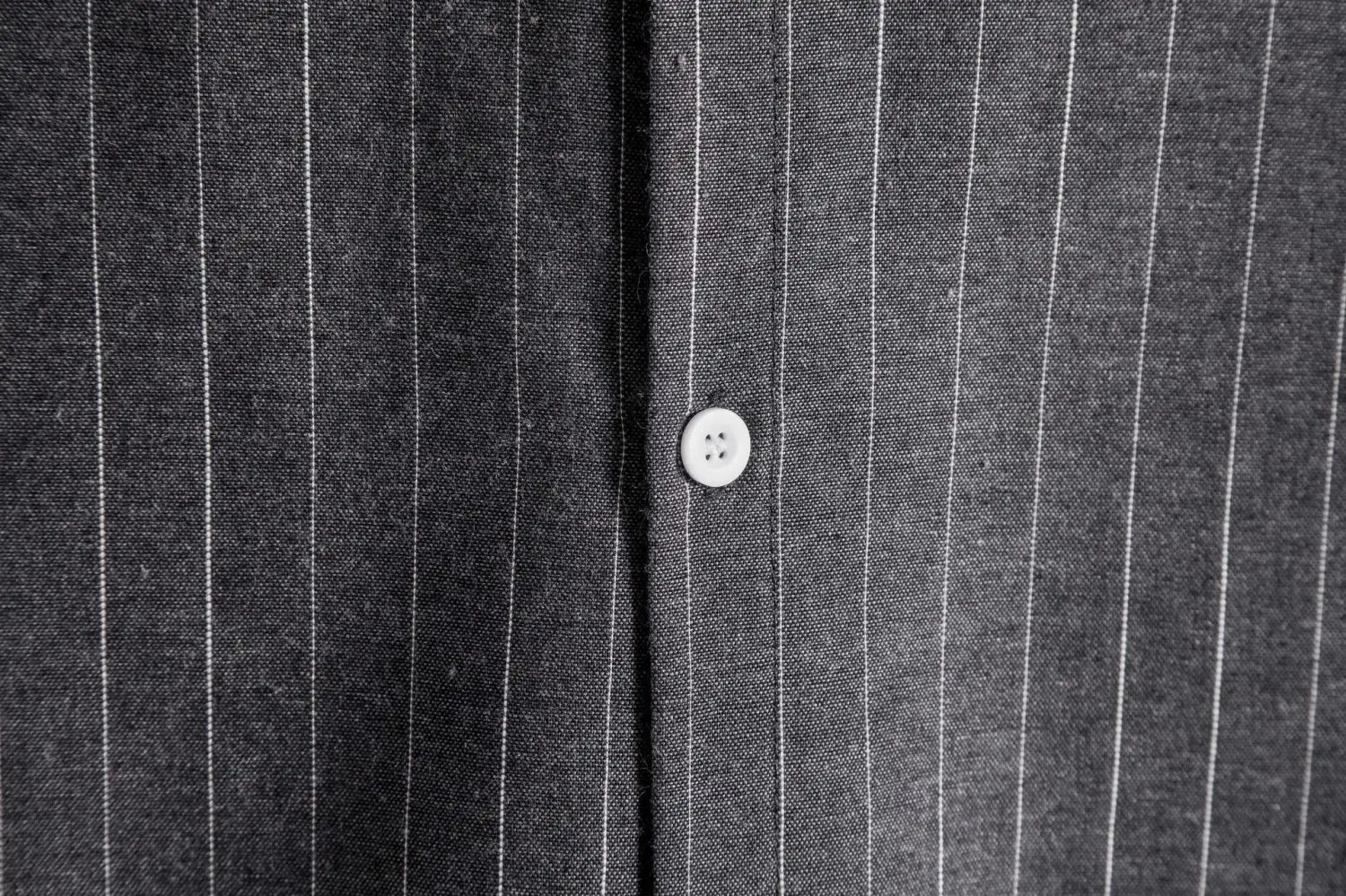 a single white four-hole button on a dark gray pinstripe fabric of a men’s slim fit pinstripe short sleeve button up shirt