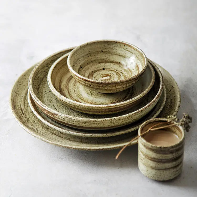 Ceramic rustic speckled stoneware tableware set featuring earthy green and beige glaze with rustic concentric rings on plates and bowls.