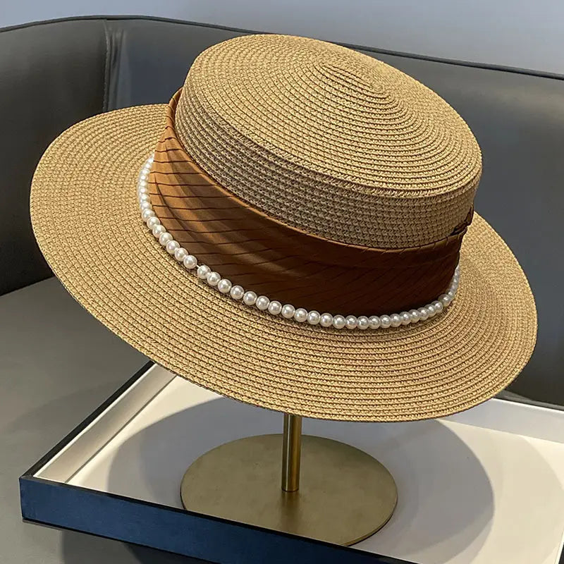 Beige straw sun hat for children with a brown satin band and a row of white pearls designed for sun protection.