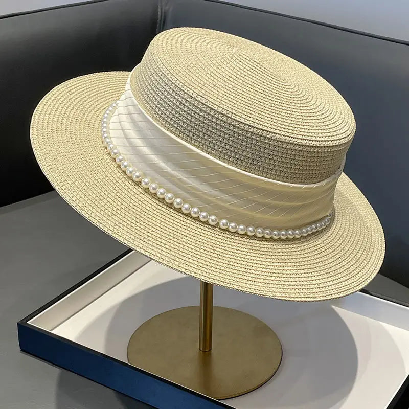 Beige straw sun hat for children with a wide brim, adorned with an ivory satin ribbon and a row of white pearls.