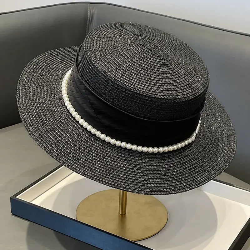 Black woven straw sun hat for children with a wide brim, adorned with a black satin ribbon and a single strand of white pearls encircling the base.