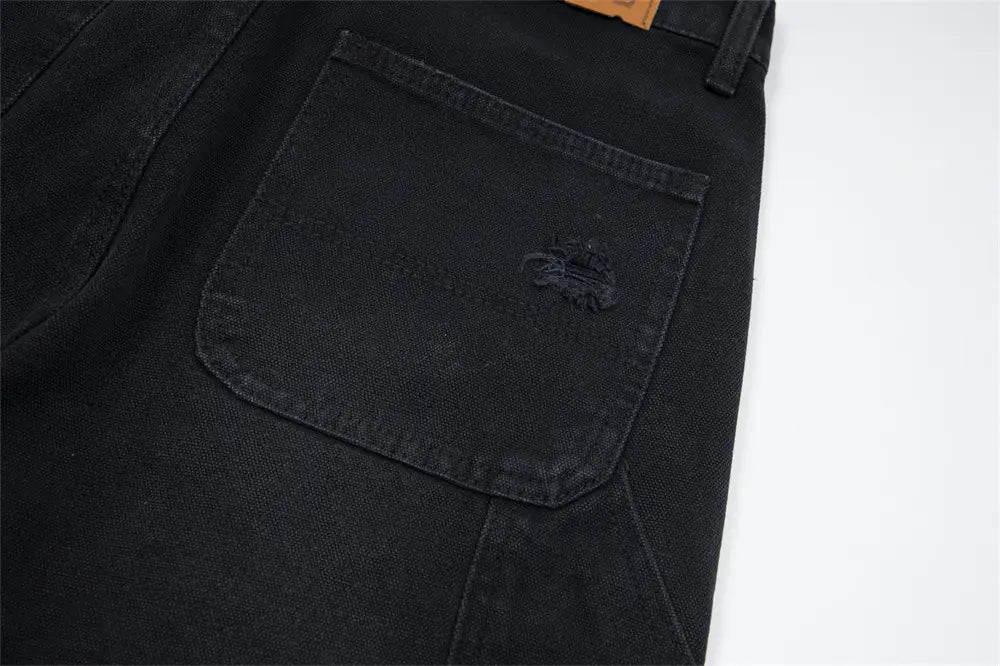 El lado posterior de los pantalones cortos de mezclilla negros para hombre, con un parche desgastado y dobladillo deshilachado, elaborado con material de mezclilla.