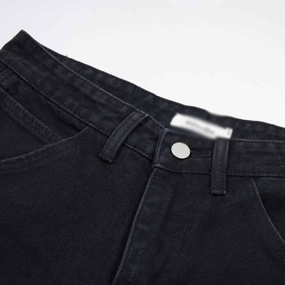 Pantalones cortos de mezclilla negros desgastados para hombre con dobladillo deshilachado, con una pretina clásica con cierre de botón plateado y detalles de costura visibles.
