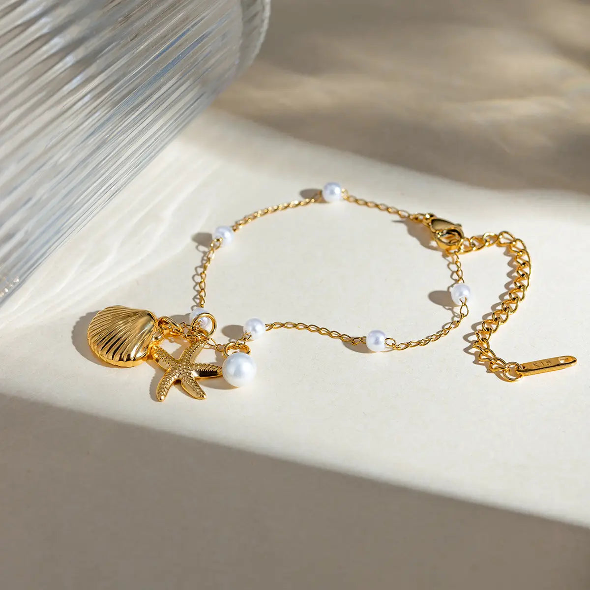 18k gold plated pearl shell and starfish charm bracelet featuring a gold-toned delicate chain with small white pearls and dangling seashell and starfish charms.