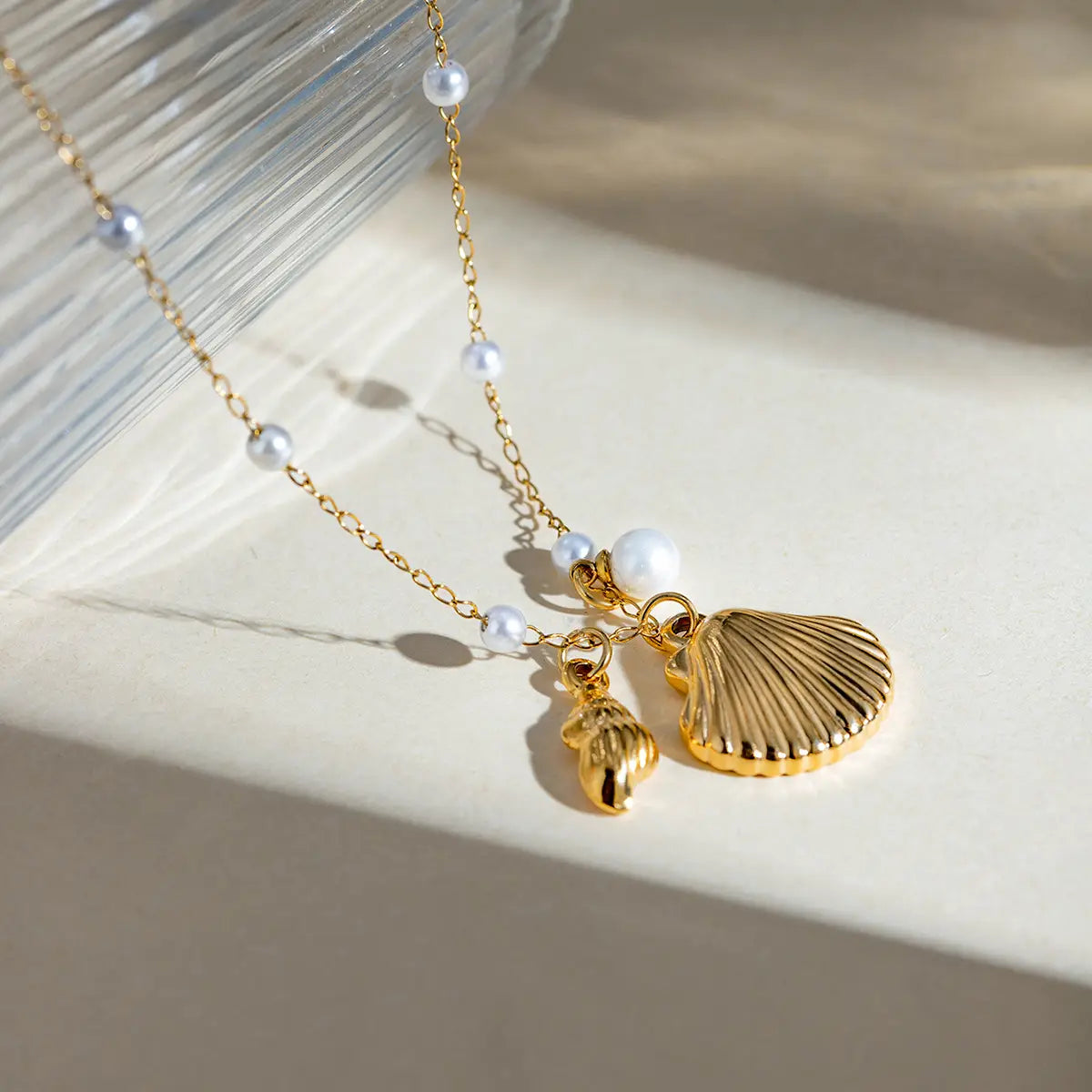 18k gold plated necklace with a delicate chain featuring small white pearls and two shell charms including a larger scallop-shaped pendant and a smaller conch-shaped charm.