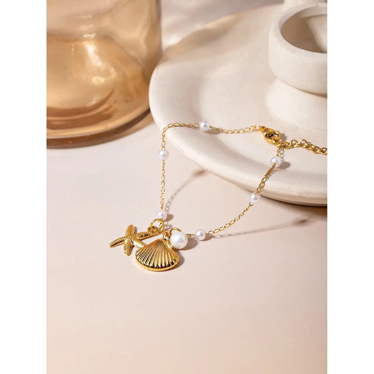 18k gold plated bracelet featuring a starfish and seashell charm accented with small pearls along the gold-toned chain.